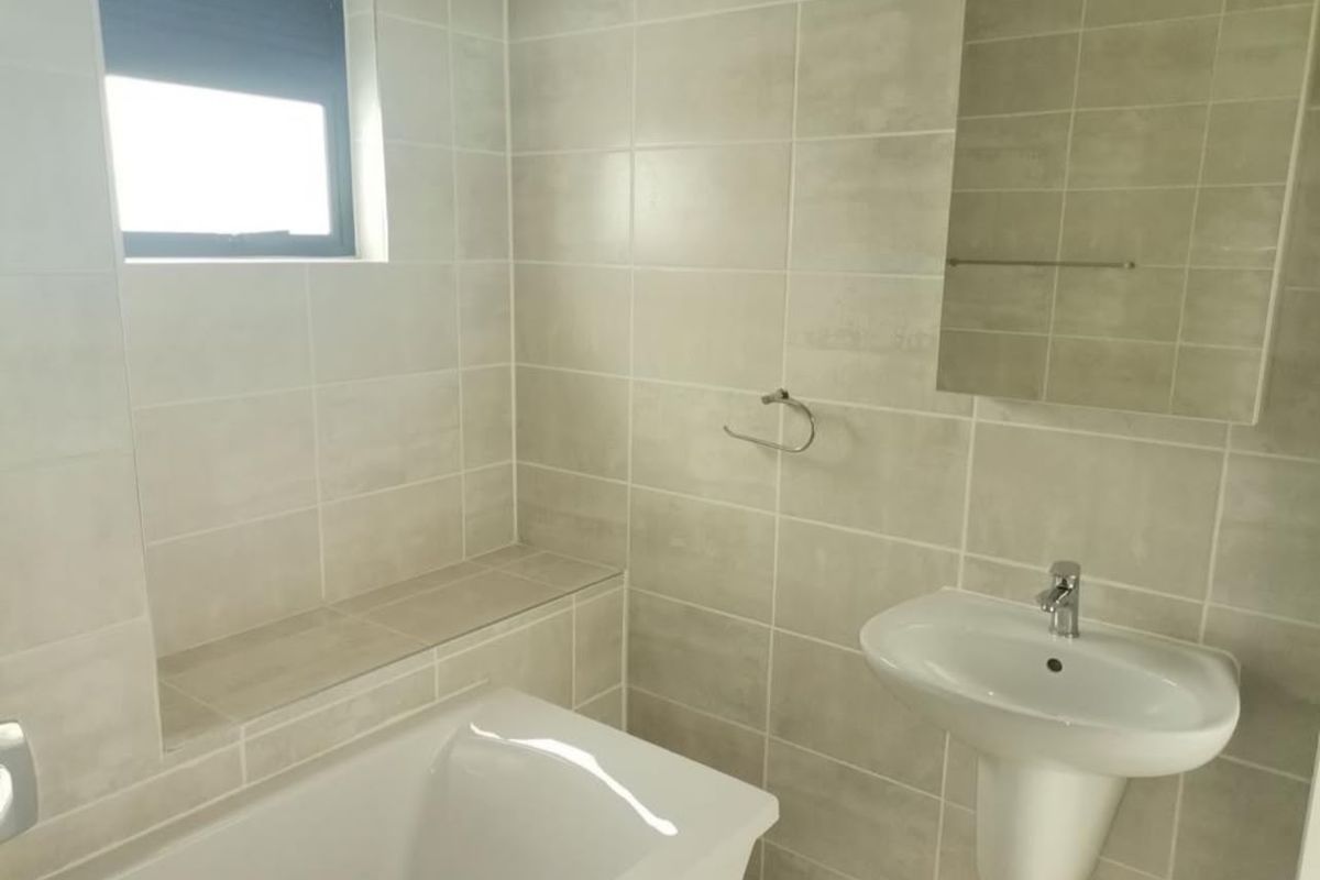 A clean, modern bathroom featuring a pedestal basin, built-in bathtub, and neutral wall tiling with a functional layout.