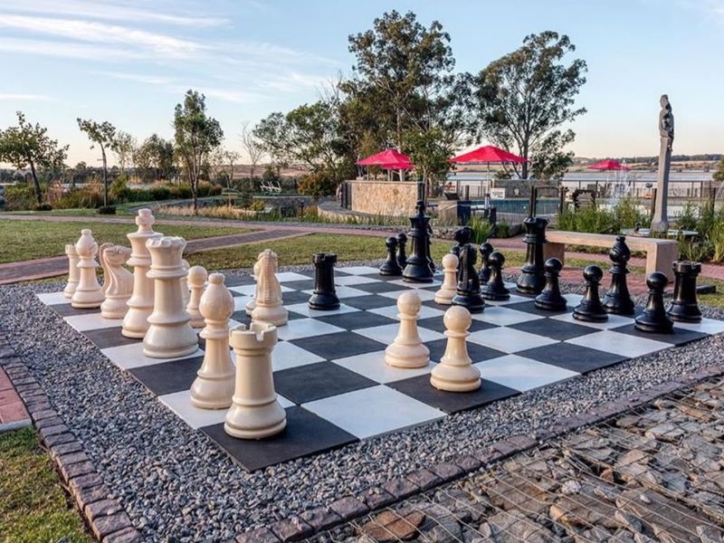 A well-maintained outdoor recreational area featuring a large garden chess set, paved walkways, and access to a communal swimming pool facility.