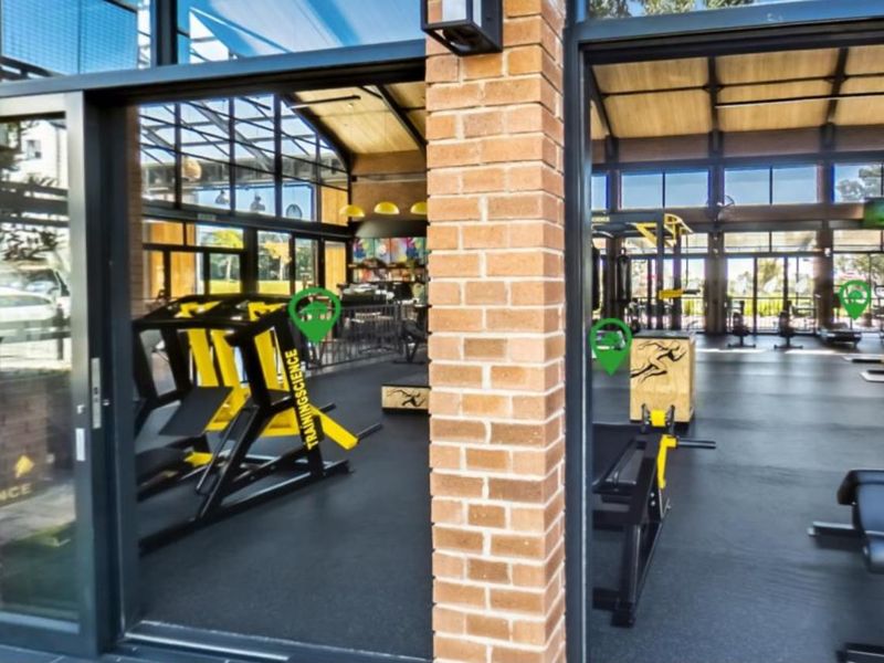 A modern, well-lit gym facility featuring exposed timber ceiling beams, large glass sliding doors, and durable rubberized flooring.