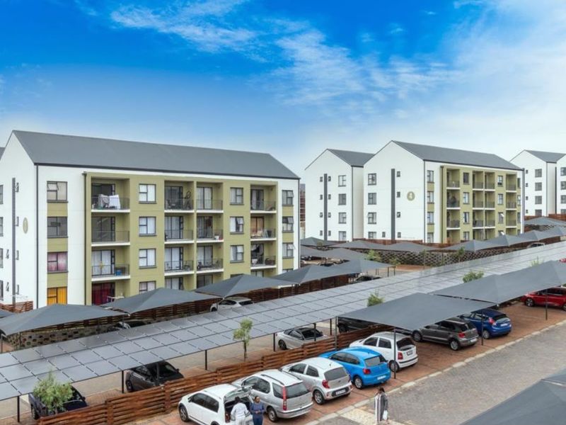 Exterior view of a modern apartment complex featuring multi-story residential blocks, private balconies, and extensive covered parking with integrated solar panels.