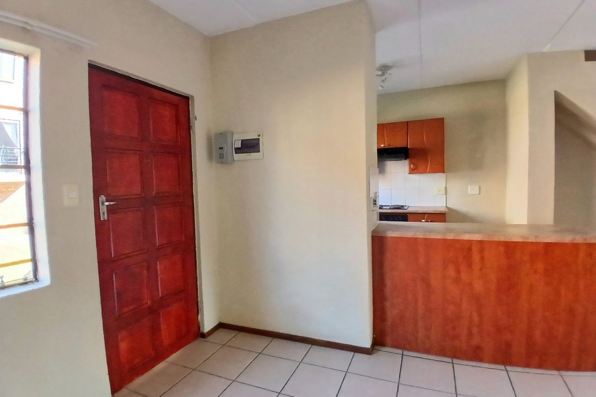 Open plan living area featuring tiled flooring, a timber entrance door, and a functional kitchen with built-in cabinetry and a breakfast counter.