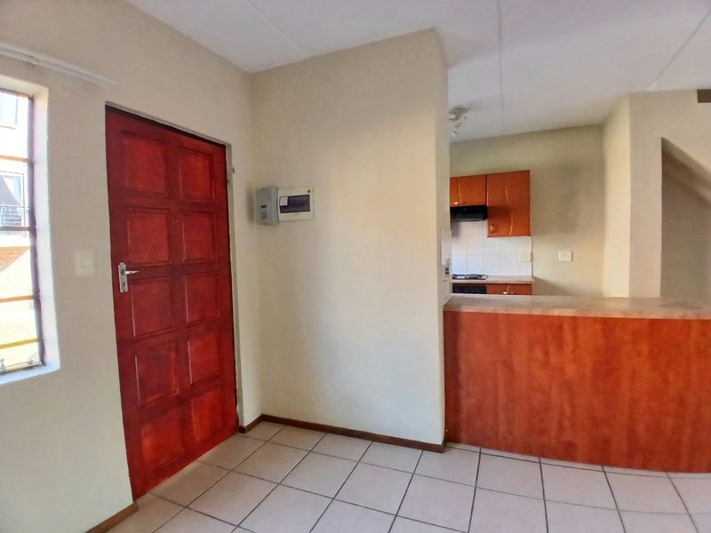 Open plan living area featuring tiled flooring, a timber entrance door, and a functional kitchen with built-in cabinetry and a breakfast counter.