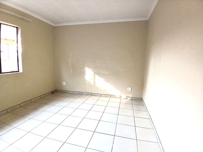 An empty bedroom featuring neutral wall paint, ceramic floor tiles, and a single window, providing a blank canvas for personalization.