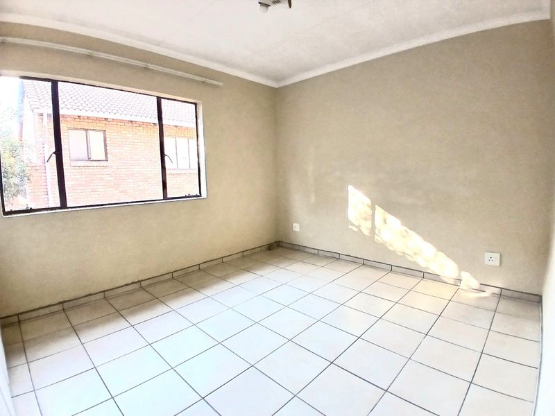 An empty bedroom featuring neutral wall paint, tiled flooring, and an aluminium-framed window providing natural light.