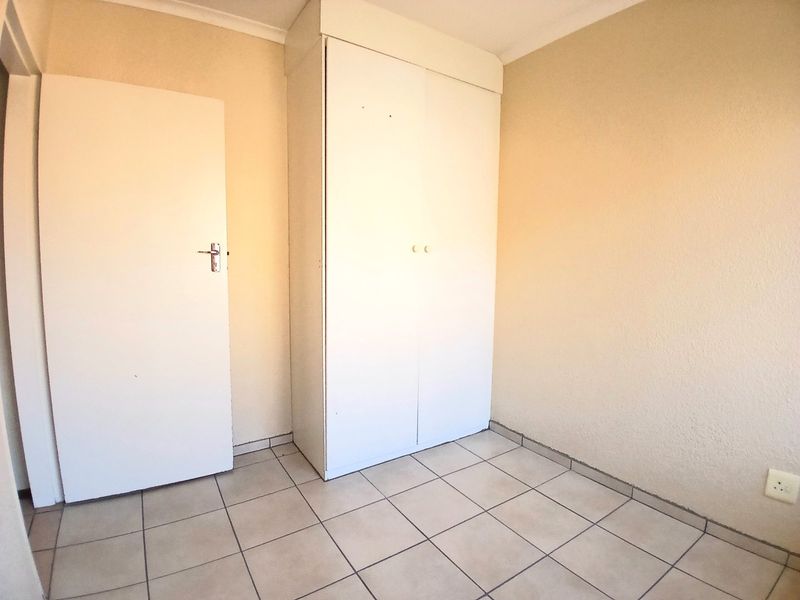 An empty bedroom featuring neutral tiled flooring and a built-in white wardrobe.