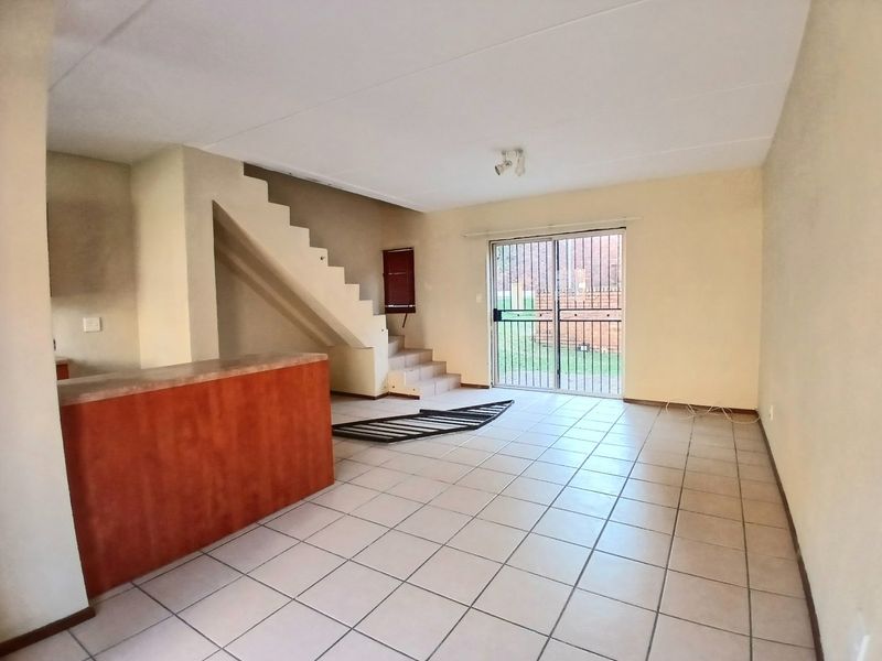 An open-plan living area featuring tiled floors, a built-in staircase, and a kitchen breakfast counter, leading out to a private outdoor space.
