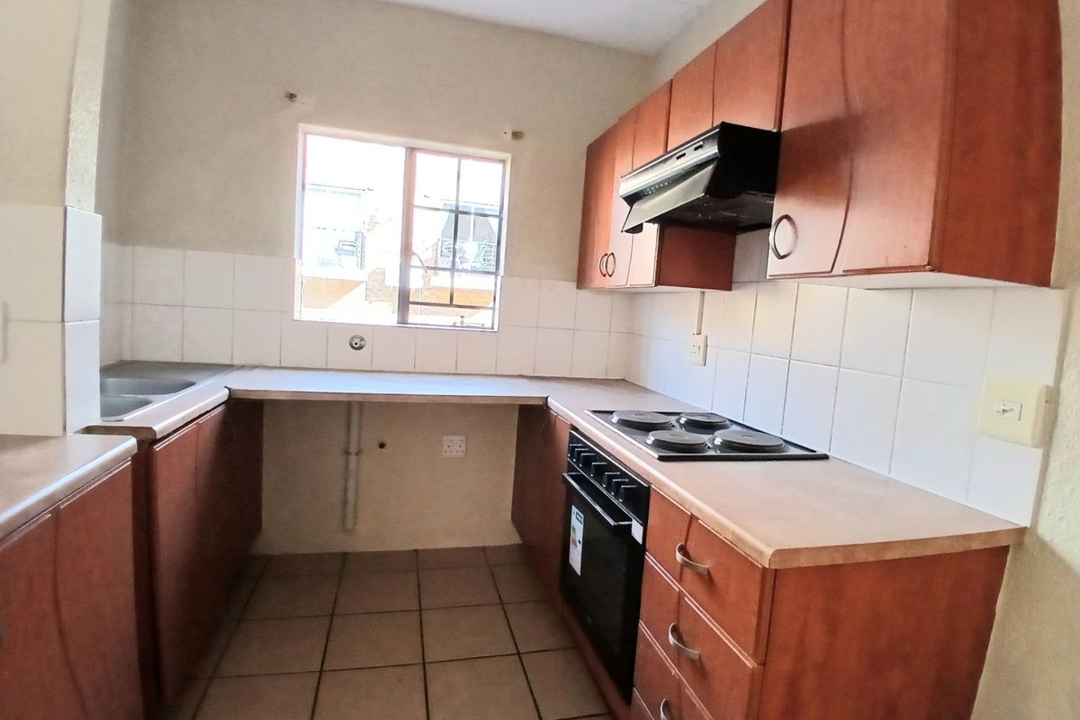 A functional kitchen featuring wooden cabinetry, laminate countertops, a built-in oven with hob, and tiled flooring, offering a practical layout for daily use.