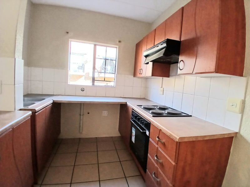 A functional kitchen featuring wooden cabinetry, laminate countertops, a built-in oven with hob, and tiled flooring, offering a practical layout for daily use.