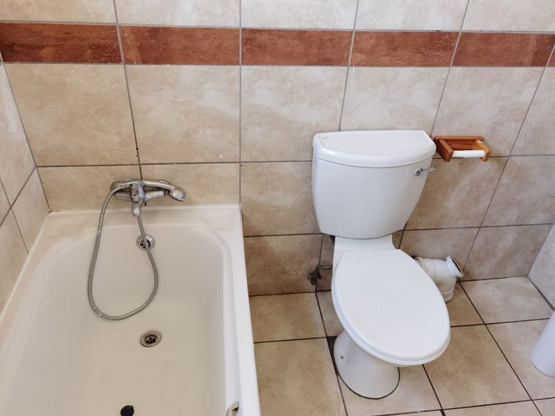 A functional bathroom featuring a standard bathtub with shower mixer and a toilet, finished with neutral wall and floor tiling.