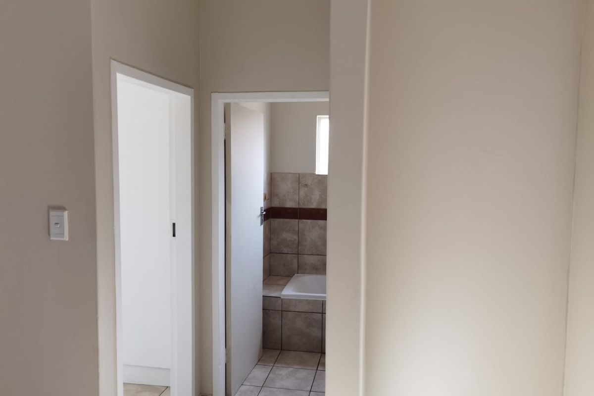 A view from a hallway looking into a bathroom featuring tiled flooring and a built-in bathtub with ceramic wall tiling.