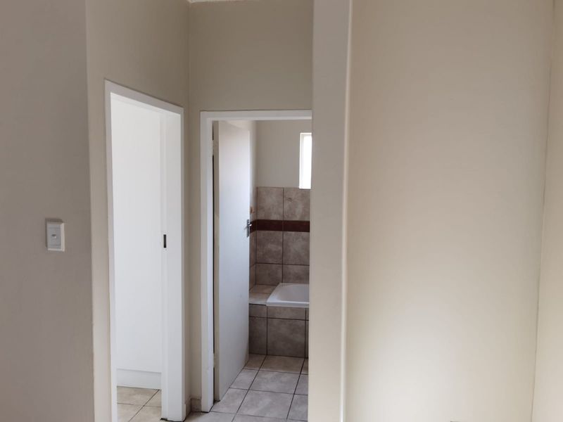 A view from a hallway looking into a bathroom featuring tiled flooring and a built-in bathtub with ceramic wall tiling.