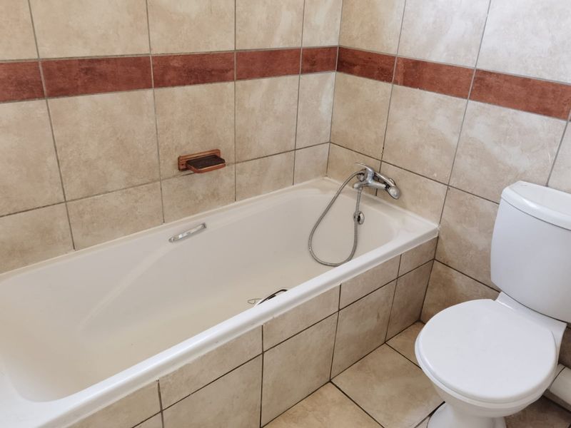A functional bathroom featuring a standard bathtub with a shower mixer, a toilet, and neutral ceramic wall and floor tiling.