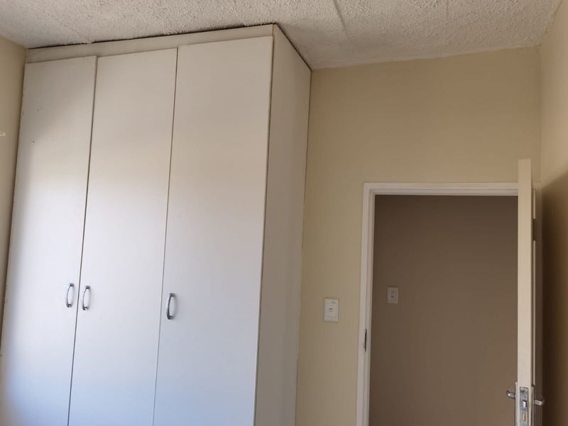 A bedroom interior featuring built-in cupboards and a textured ceiling, showing signs of wear and requiring cosmetic updates.