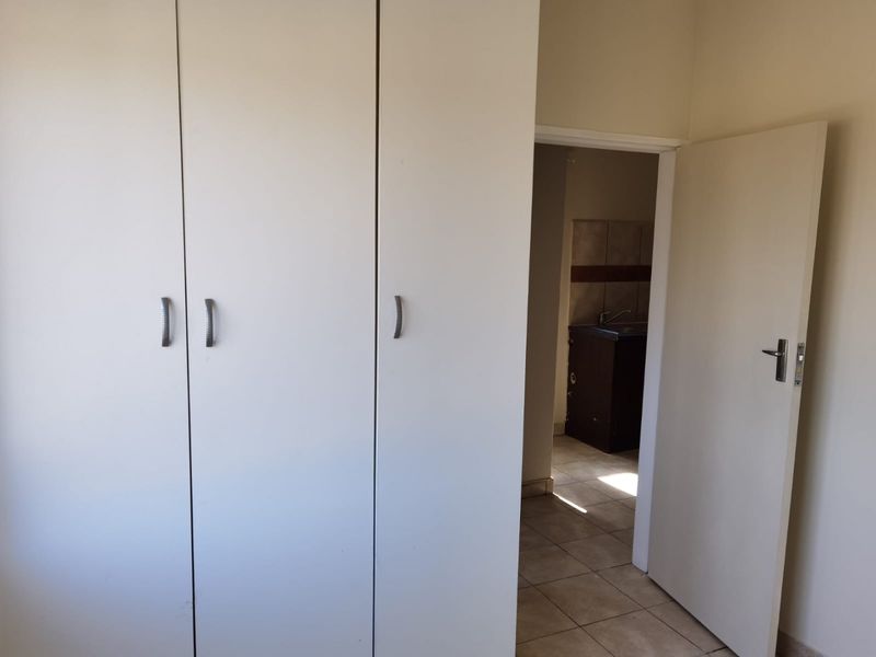 A clean, empty bedroom featuring built-in cupboards and tiled flooring, with a view through the doorway into an adjacent tiled utility or kitchen area.