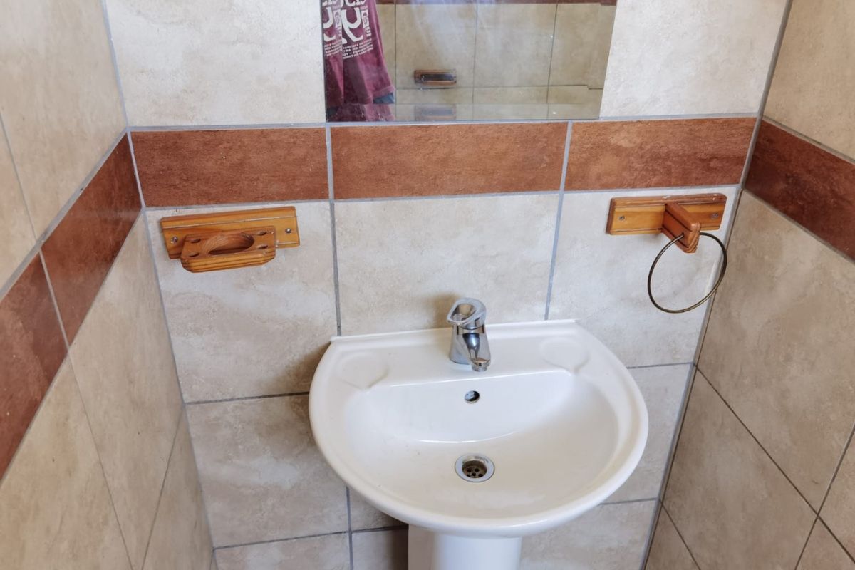 A compact bathroom featuring a white pedestal basin, chrome mixer tap, and neutral wall tiling with a decorative accent border.