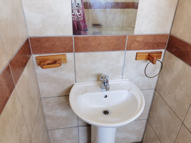 A compact bathroom featuring a white pedestal basin, chrome mixer tap, and neutral wall tiling with a decorative accent border.