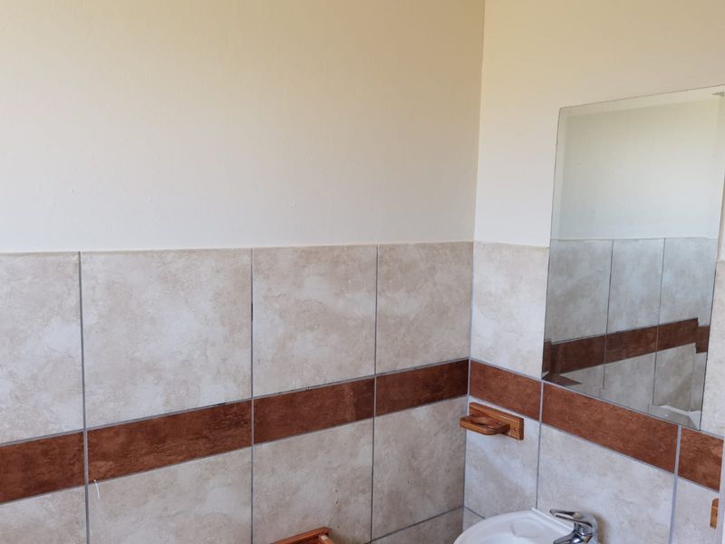A functional bathroom space featuring neutral ceramic wall tiles with a decorative accent border, a wall-mounted mirror, and a standard washbasin.