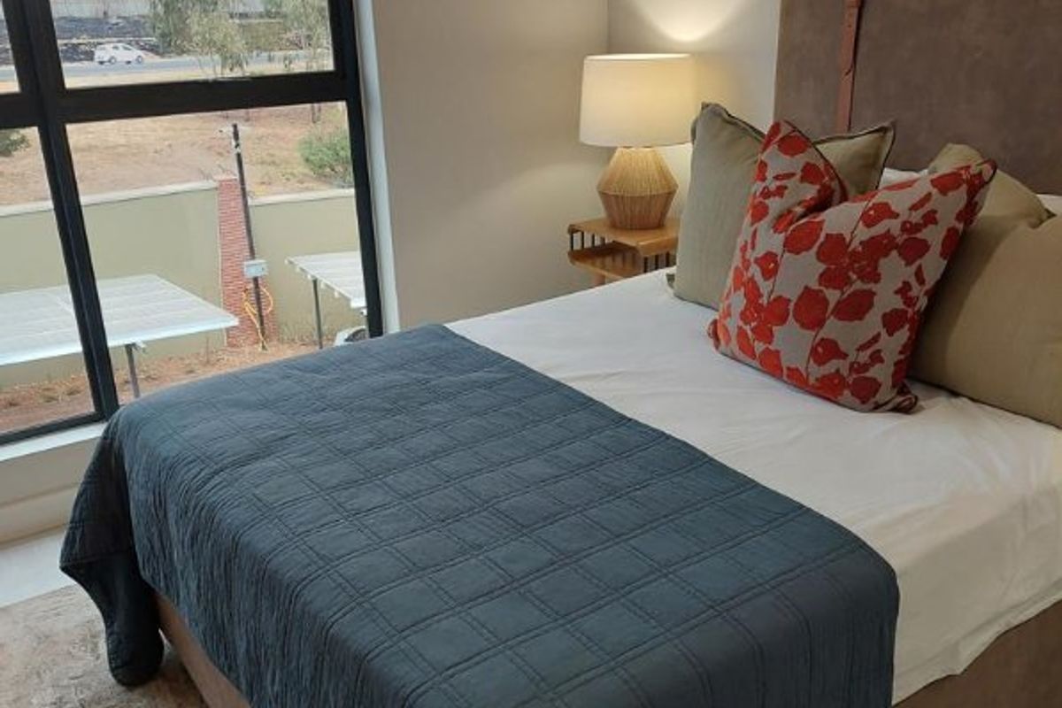A well-lit bedroom featuring a large window with views, neutral wall finishes, and modern architectural framing.