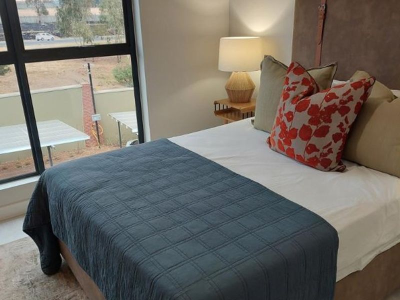 A well-lit bedroom featuring a large window with views, neutral wall finishes, and modern architectural framing.