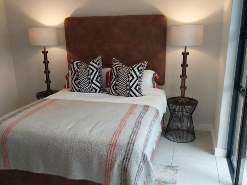 A well-maintained bedroom featuring neutral tiled flooring, a modern pendant light, and a large sliding glass door providing natural light.
