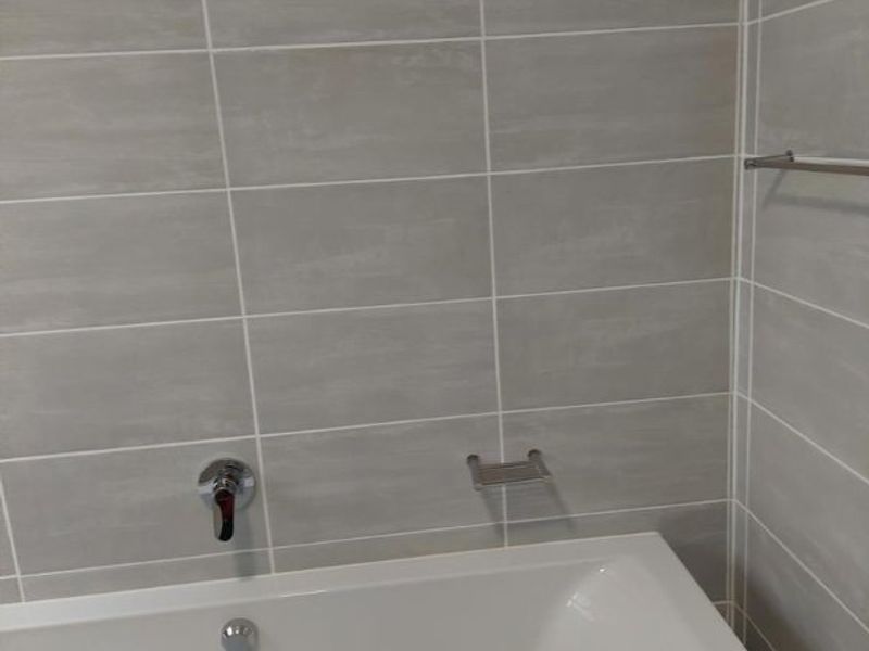 A clean, modern bathroom featuring a built-in bathtub with chrome fixtures and neutral grey wall tiling.