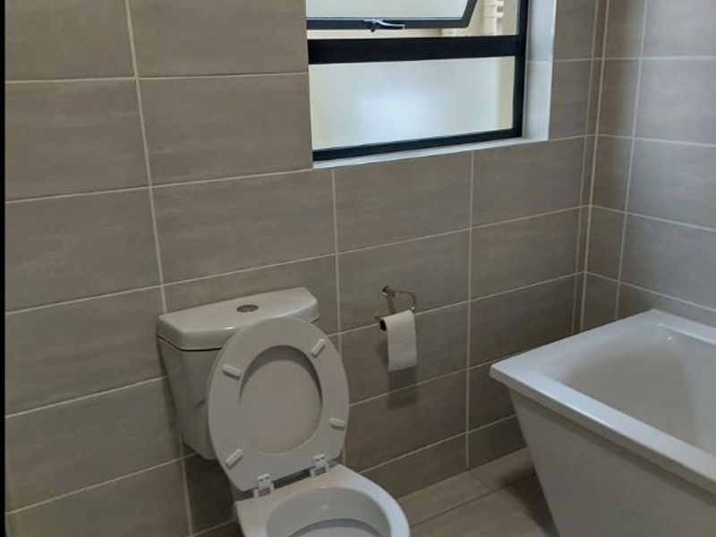 A clean, modern bathroom featuring neutral wall and floor tiles, a white bathtub, and a top-hung window for natural ventilation.