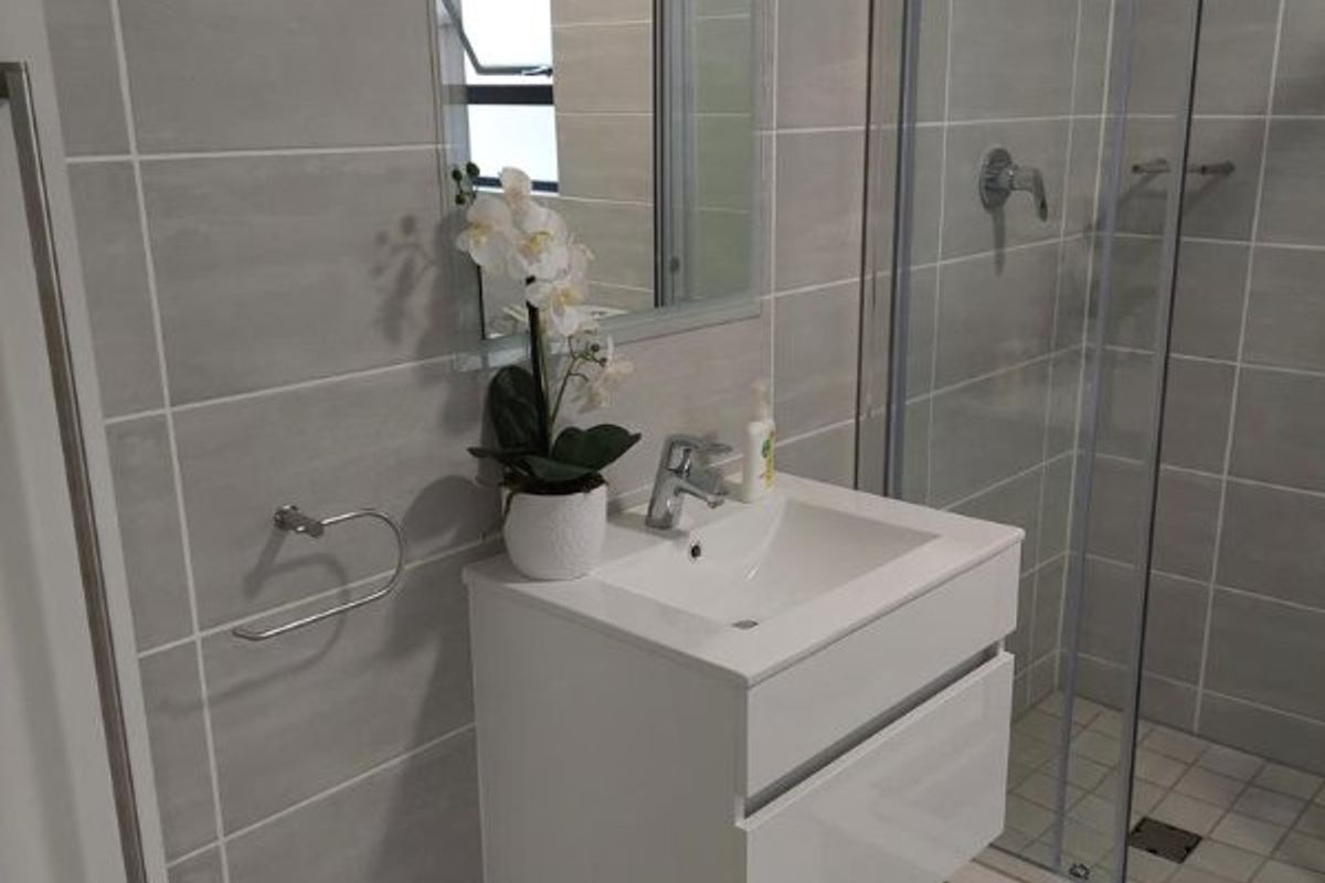 Modern bathroom featuring a wall-mounted vanity with basin, a glass-enclosed shower, and neutral grey floor-to-ceiling wall tiles.