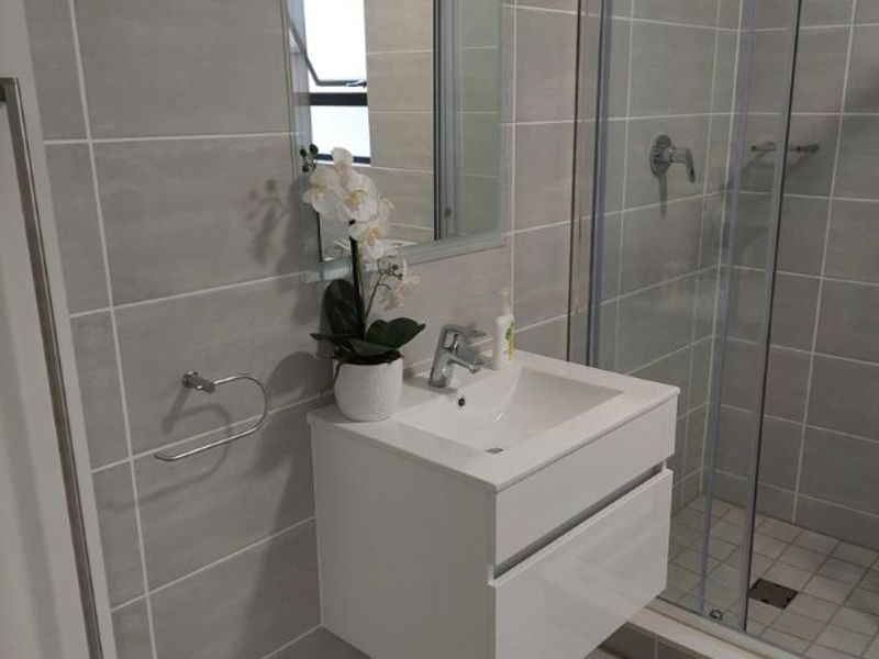 Modern bathroom featuring a wall-mounted vanity with basin, a glass-enclosed shower, and neutral grey floor-to-ceiling wall tiles.