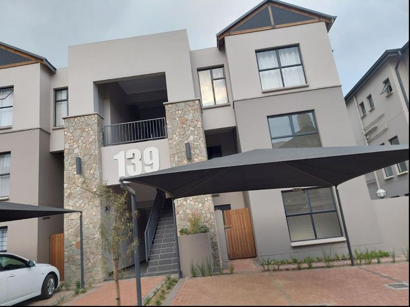 Front elevation of a modern multi-story apartment building featuring stone cladding, a paved driveway, and integrated shade sail parking.