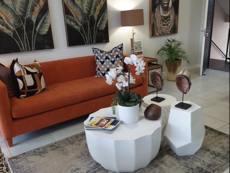 A well-maintained living room featuring neutral tiled flooring and a clean, modern aesthetic with direct access to an internal hallway.