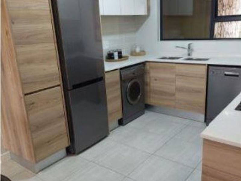 Modern kitchen featuring wood-grain cabinetry, stone countertops, double sink, and tiled flooring with integrated appliance spaces.