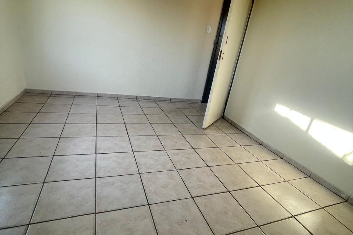An empty bedroom featuring neutral wall paint and ceramic floor tiles, providing a blank canvas for potential interior design updates.