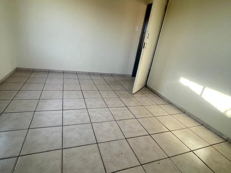 An empty bedroom featuring neutral wall paint and ceramic floor tiles, providing a blank canvas for potential interior design updates.