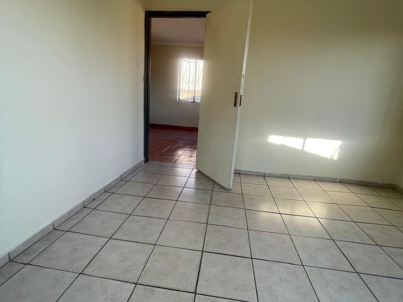 An empty bedroom featuring neutral tiled flooring and a doorway leading to an adjacent room with a window.