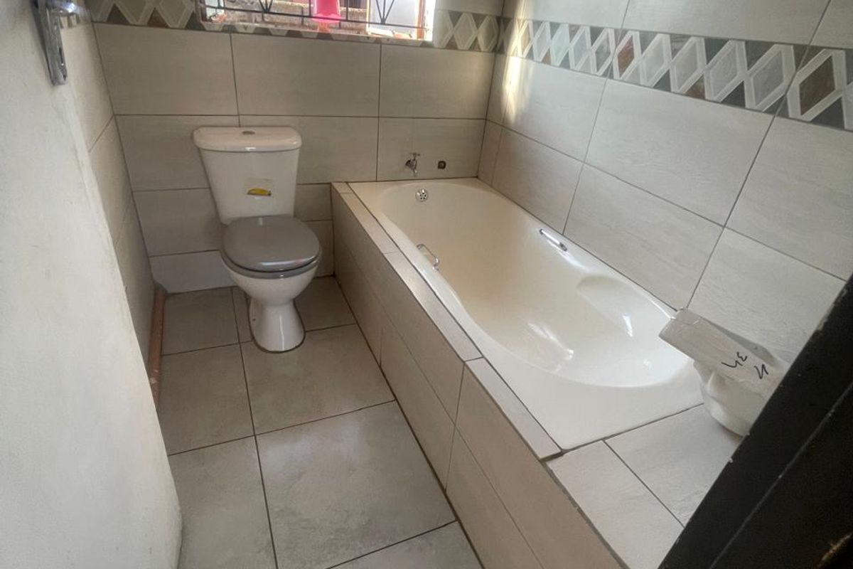 A compact bathroom featuring a built-in bathtub, toilet, and neutral wall tiling with a decorative border.