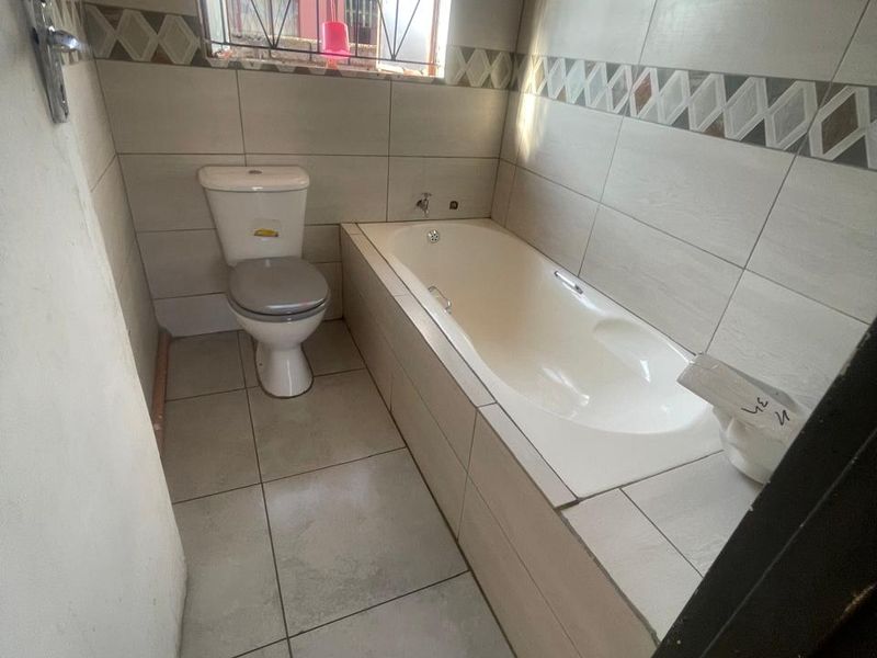 A compact bathroom featuring a built-in bathtub, toilet, and neutral wall tiling with a decorative border.