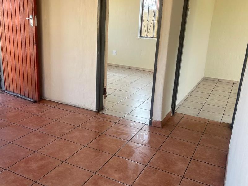 An empty hallway featuring terracotta-style ceramic floor tiles and access to adjacent rooms through standard door frames.