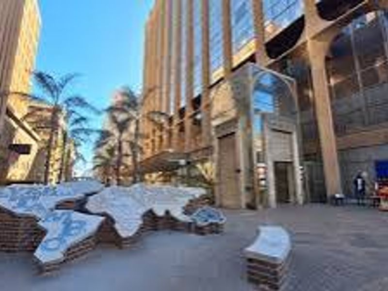 A wide-angle view of a commercial building exterior featuring a paved plaza, glass facade, and a decorative brick map installation.