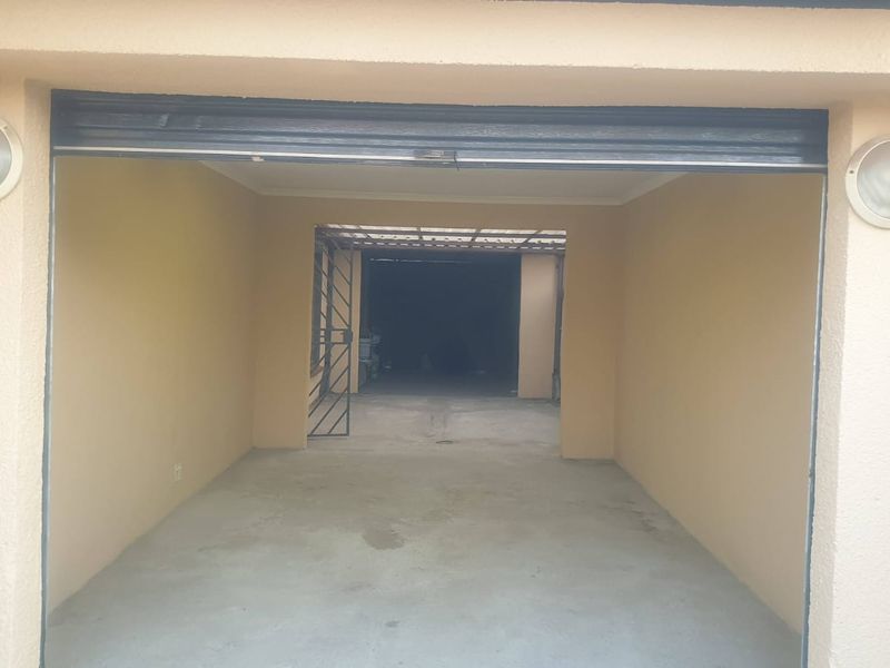 A spacious, empty garage featuring a concrete floor, exterior wall-mounted lighting, and a security gate leading to the rear area.