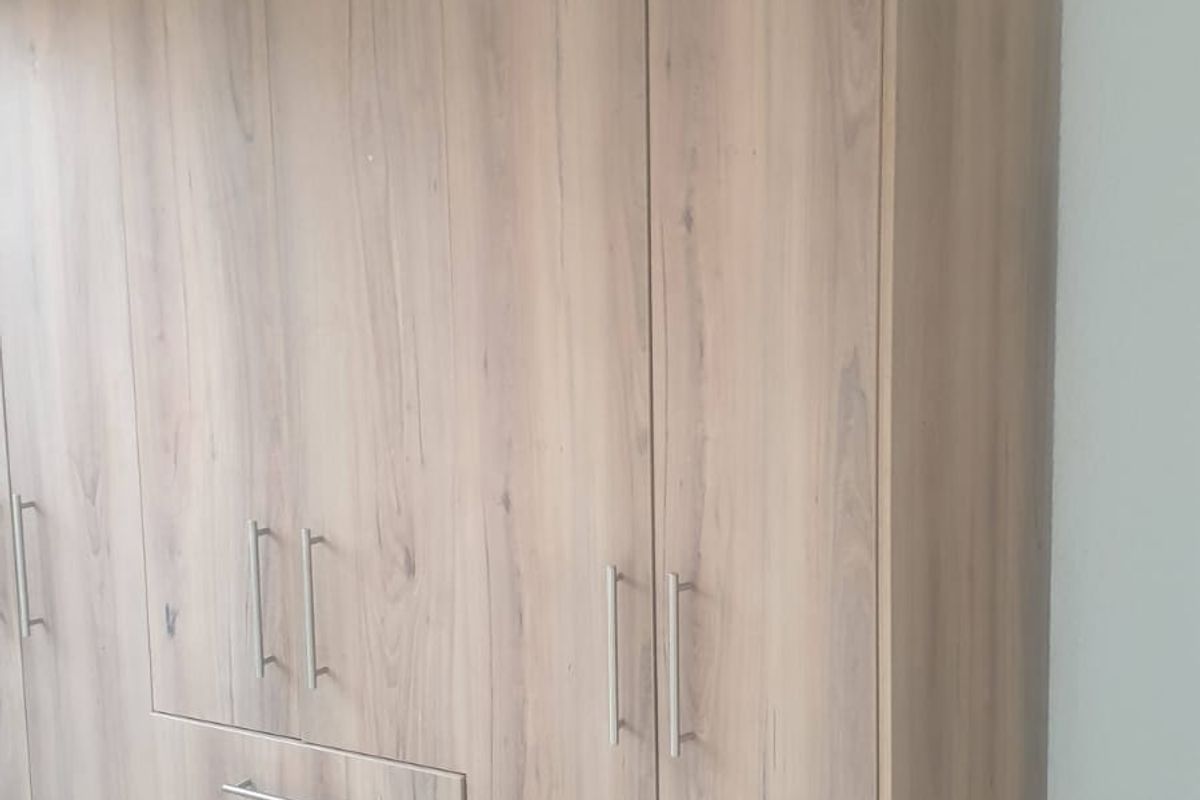 A bedroom featuring a large, modern wood-finish built-in wardrobe with integrated drawers and stainless steel handles, set against tiled flooring.