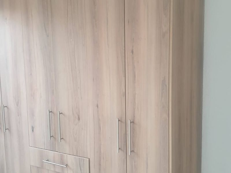 A bedroom featuring a large, modern wood-finish built-in wardrobe with integrated drawers and stainless steel handles, set against tiled flooring.