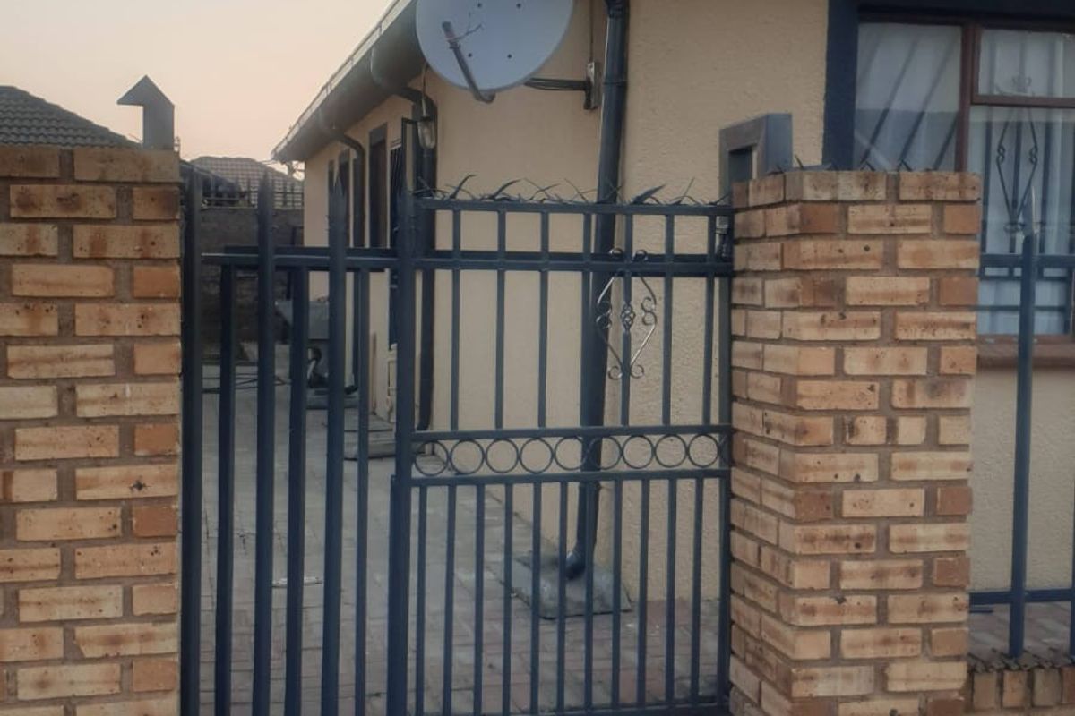 Front exterior view of the property featuring a brick boundary wall, metal security gate, and paved driveway access.