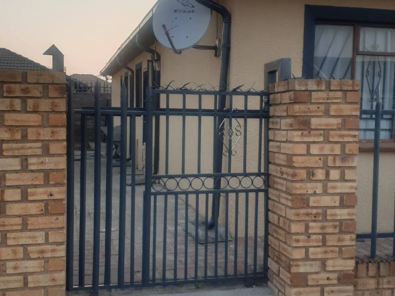 Front exterior view of the property featuring a brick boundary wall, metal security gate, and paved driveway access.