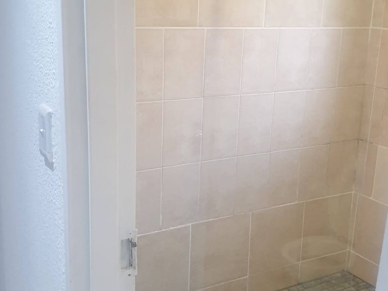 A clean walk-in shower featuring neutral wall tiles, a textured pebble floor, and a modern overhead rain shower head.