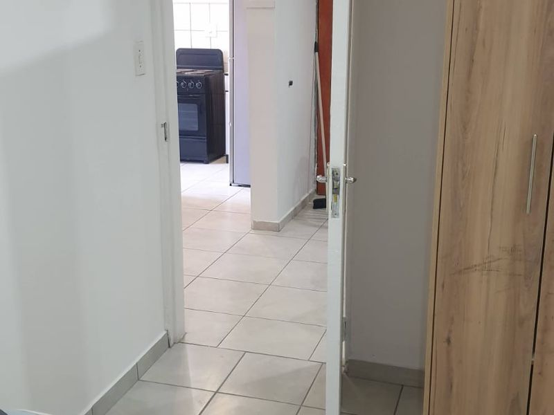 A view from a bedroom looking through a hallway towards the kitchen area, featuring tiled flooring and a built-in wooden cupboard.