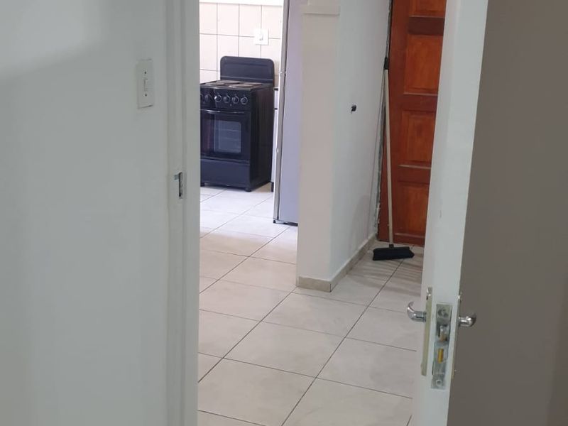 A view through a doorway into a tiled hallway leading to a kitchen area with a built-in stove.
