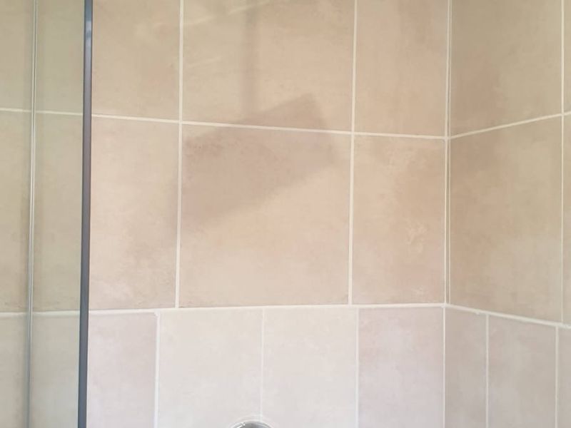 A clean, modern shower enclosure featuring neutral ceramic wall tiles, a square rainfall shower head, and a glass screen.