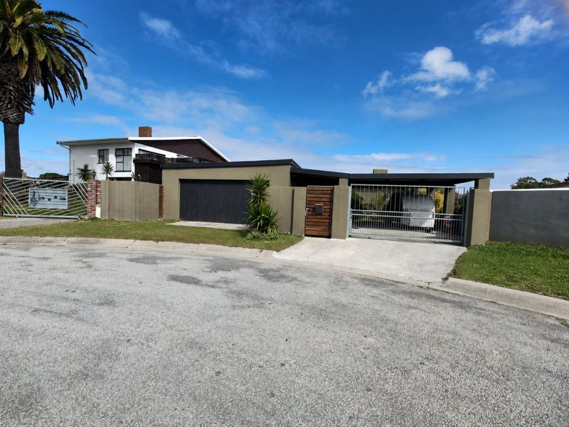Front elevation of the property featuring a secure garage, carport, and gated entrance with established perimeter fencing.