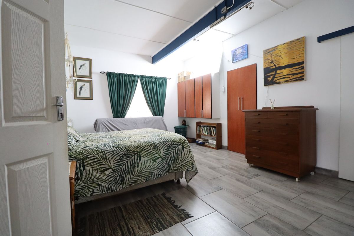 A spacious bedroom featuring tiled flooring, built-in wooden cupboards, and an exposed ceiling beam, offering a functional layout with ample storage space.