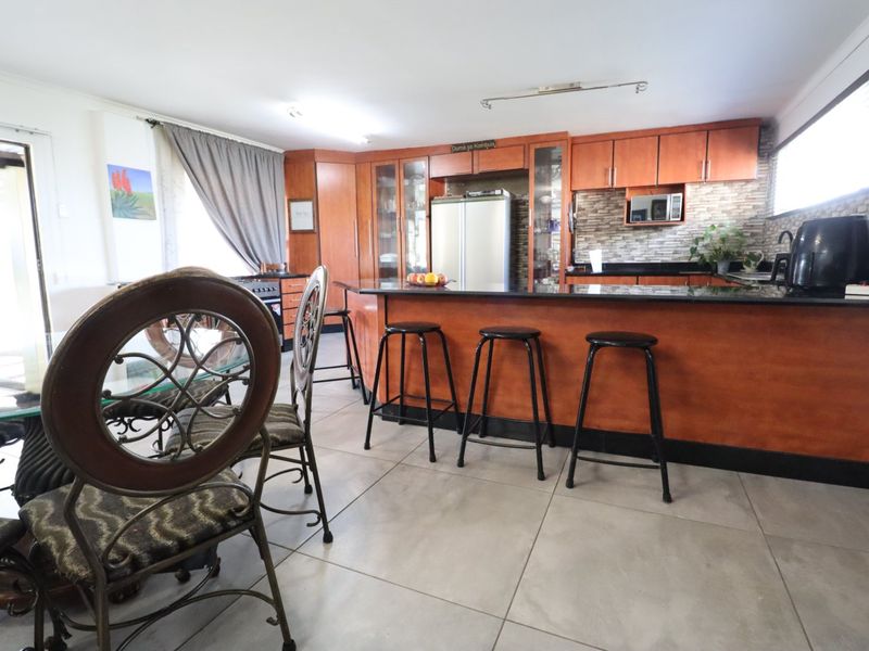 Open-plan kitchen and dining area featuring wooden cabinetry, granite countertops, a breakfast bar, and neutral tiled flooring.